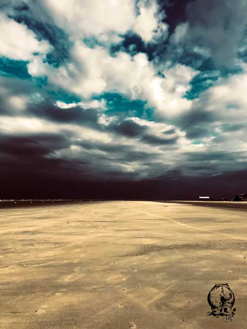 Menschenleerer Strand in Sankt Peter Ording, im Winter. Dunkle Wolken, im Hintergrund ziehen schwarze Regenwolken auf