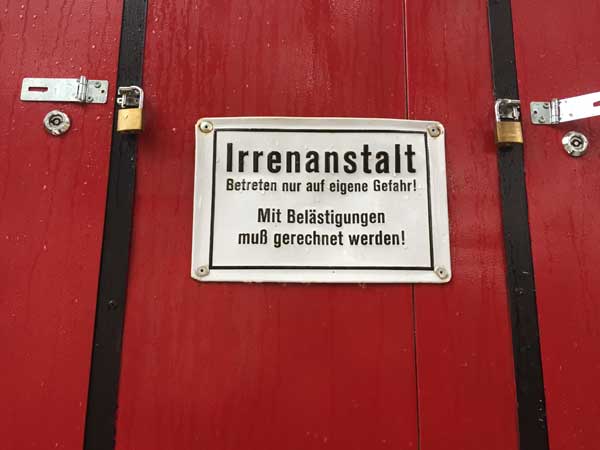 Bild mit einem Schild, darauf steht: Irrenanstalt Betreten auf eigene Gefahr. Mit Belästigung muss gerechnet werden